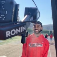 Student athlete standing on track and smiling for a camera.