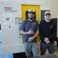 Welding students Justin Adams and Colin DeGross pose in front of a piece of equipment in the newly renovated Shops building