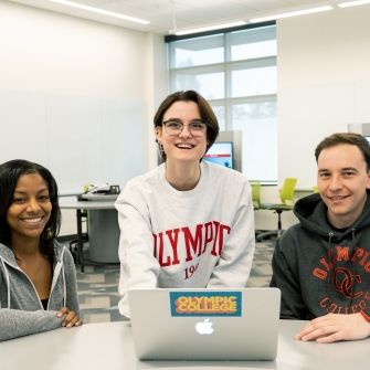 Three students sitting at a table in front of a laptop computer