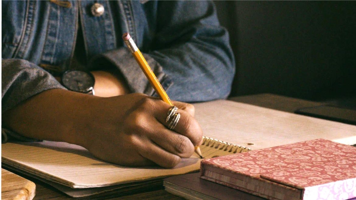 Person of color with feather ring writing in a journa