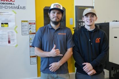 Welding students Justin Adams and Colin DeGross pose in front of a piece of equipment in the newly renovated Shops building